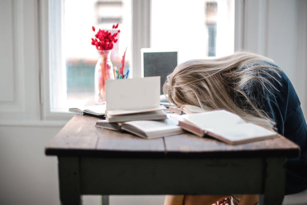 Person with head down on a desk with books and a laptop