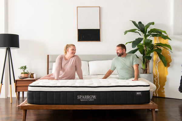 Two people sitting on a sparrow mattress smiling at eachother