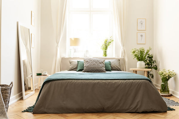 Neatly made bed with green and brown bedding in a bright bedroom.