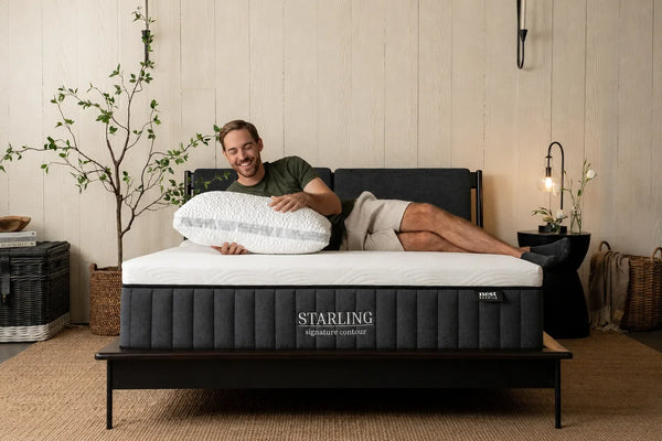 a man laying across the starling mattress with a pillow in his arms
