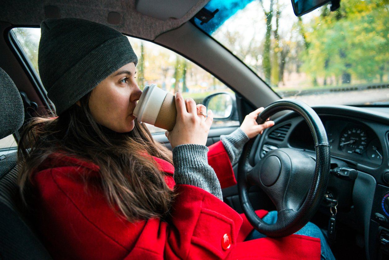 woman driving on a road trip and sipping coffee in autumn coat