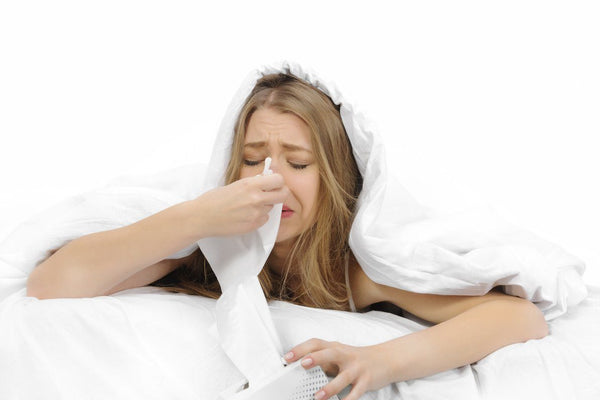 young woman blowing nose in bed