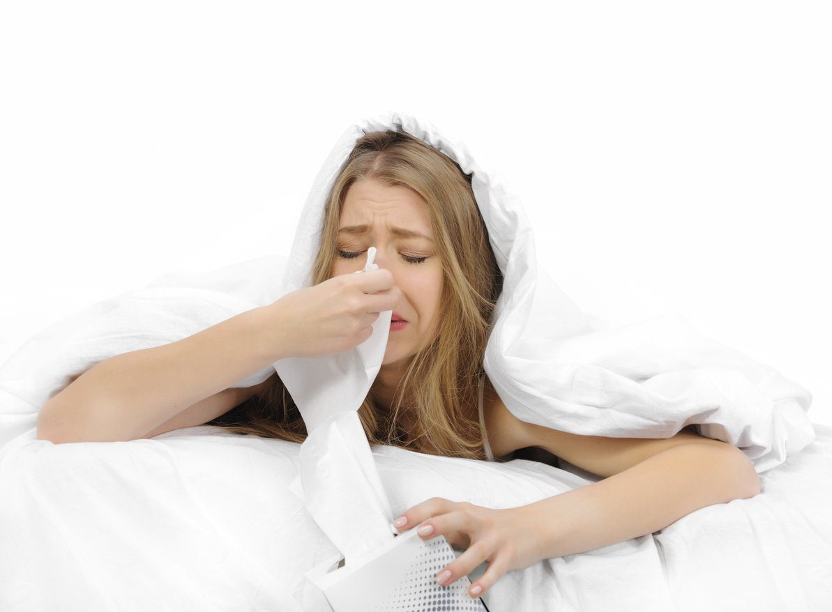 young woman blowing nose in bed