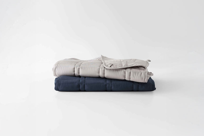 Two folded weighted blankets, one silver sage and one luna blue, on a white background