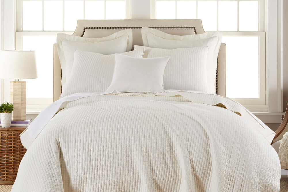 Neatly made bed with cream cross stitch quilt bedding in a bright bedroom.
