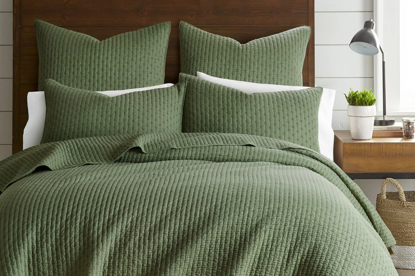 Green textured cross stitch quilt bedding set on a bed with matching pillows in a bedroom setting.