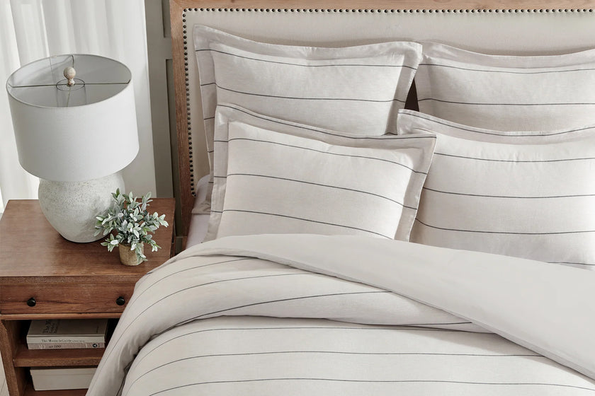 Neatly made bed with striped bedding, nightstand with lamp and plant, and wooden headboard.