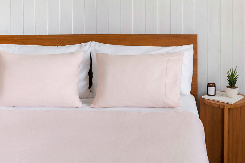 Neatly made bed with blush pink linen bedding and pillows against a wooden headboard.