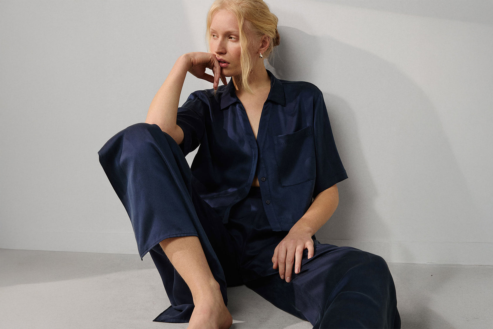 Woman wearing a deep blue silk pajama set sitting against a light gray background