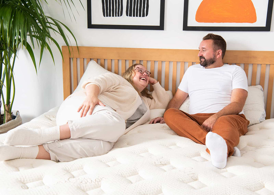 couple smiling at each other on a mattress in their bedroom